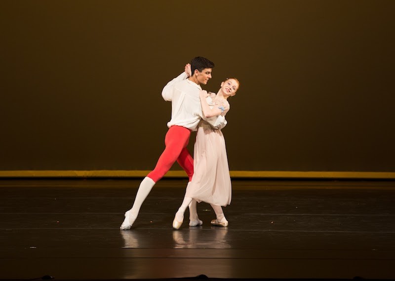 Two Dancers hold one another as if they are going to engage in a waltz. His foot points behind him while her foot points to the front.